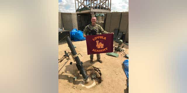 SPC George Kemper holds a Loyola Academy flag while serving in the U.S. Army.
