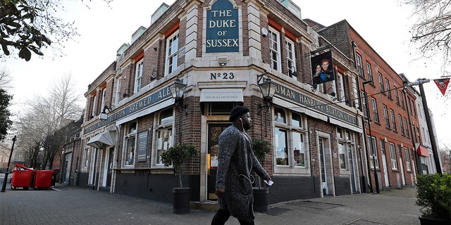 A man walks past the Duke of Sussex pub with a sign depicting the image of Britain's Prince Harry and his wife Meghan, near Waterloo station, London, Tuesday March 9, 2021.  (AP Photo/Frank Augstein)