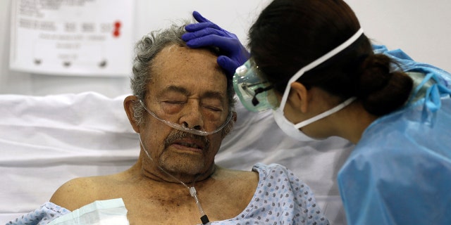 A healthcare worker strokes the forehead of a COVID-19 patient in a field hospital set up inside the Citibanamex convention center in Mexico City, on the first year anniversary that the World Health Organization declared the coronavirus a pandemic. (AP Photo/Fernando Llano, File)