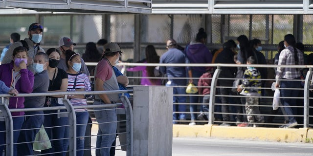 Travelers, left, queuing to cross a customs area in the United States at the McAllen-Hidalgo International Bridge, watch a group of migrants, right, being deported to Reynosa, Mexico.  (AP Photo / Julio Cortez)