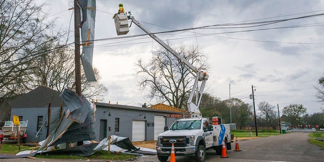 Un travailleur des services publics cherche à réparer les lignes avec le toit de Kelley Electric drapé sur les lignes après que le centre-ville de Moundville a été frappé par des intempéries, le mercredi 17 mars 2021, à Moundville, en Alabama. dans le comté rural de Chilton et dans les communautés de Burnsville et de Moundville en Alabama, où l'électricité était coupée et les arbres bloquaient une autoroute principale.  (Photo AP / Vasha Hunt)