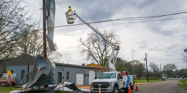 Un travailleur des services publics cherche à réparer les lignes avec le toit de Kelley Electric drapé sur les lignes après que le centre-ville de Moundville a été frappé par des intempéries, le mercredi 17 mars 2021, à Moundville, en Alabama. dans le comté rural de Chilton et dans les communautés de Burnsville et de Moundville en Alabama, où l'électricité était coupée et les arbres bloquaient une autoroute principale.  (Photo AP / Vasha Hunt)