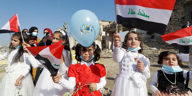 Children in their festive garment wave Iraqi flags to the camera as they arrive to join Pope Francis who will pray for the victims of war at Hosh al-Bieaa Church Square, in Mosul, Iraq, once the de-facto capital of IS, Sunday, March 7, 2021. (Associated Press)