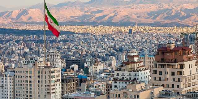 Waving the flag of Iran over the Tehran skyline at sunset. 