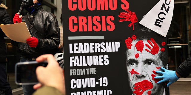 A person places his red painted hands on a poster of Gov. Andrew Cuomo's book as people gather outside of his NYC office to protest against cuts to health care on March 01, 2021 in New York City. (Photo by Michael M. Santiago/Getty Images)