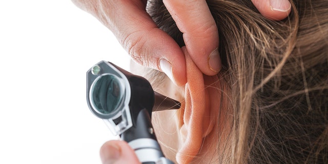 Closeup of examining ear with an otoscope