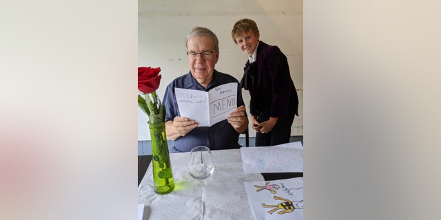 In this Aug, 2020, photo provided by courtesy of Nancy Peters, Joe Peters reads the menu on his birthday in a garage served by grandson, Nate Hoying, right, in Cincinnati.