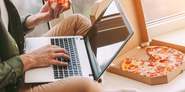 Closeup stylish businessman freelancer eat slice of tasty pizza and using laptop for work from home.
