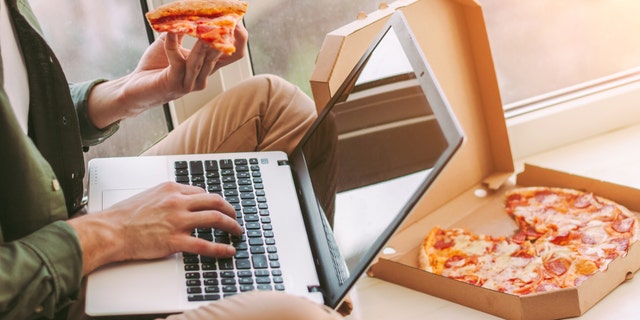 Closeup stylish businessman freelancer eat slice of tasty pizza and using laptop for work from home.