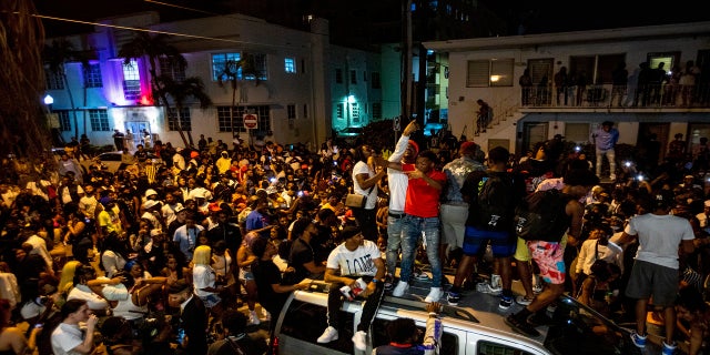 Crowds defiantly gather in the street while a speaker blasts music an hour past curfew in Miami Beach, Fla., on Sunday. An 8 p.m. curfew has been extended in Miami Beach after law enforcement worked to contain unruly crowds of spring break tourists. (AP/Miami Herald)