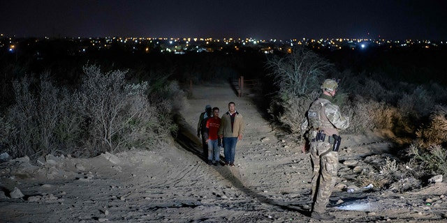 Illegal immigrants who arrived across the Rio Grande river from Mexico make their way along a track past a US border patrol agent on March 27, 2021 towards a makeshift processing checkpoint before being detained at a holding facility, in the border city of Roma. (Photo by Ed JONES / AFP) (Photo by ED JONES/AFP via Getty Images)