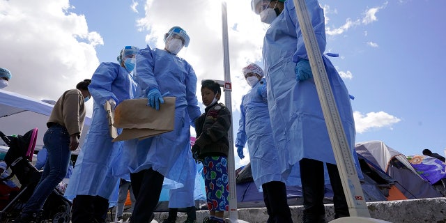 Baja California state health workers measure the height of a boy at a makeshift camp for migrants seeking asylum in the United States at the border crossing Friday, 行進 12, 2021, ティファナで, メキシコ. (AP写真/グレゴリーブル)