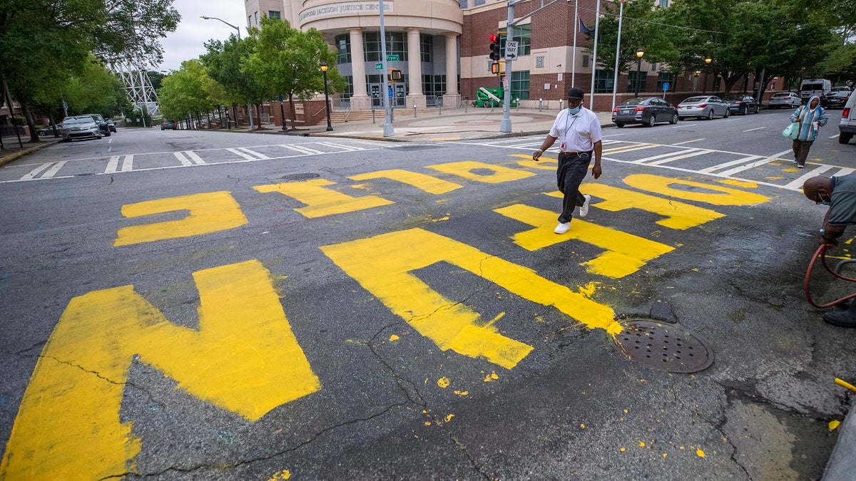 In this Wednesday, June 10, 2020, file photo, a man walk across a "Defund Police" written in front of the Atlanta Police Department Headquarters. (Alyssa Pointer/Atlanta Journal-Constitution via AP)