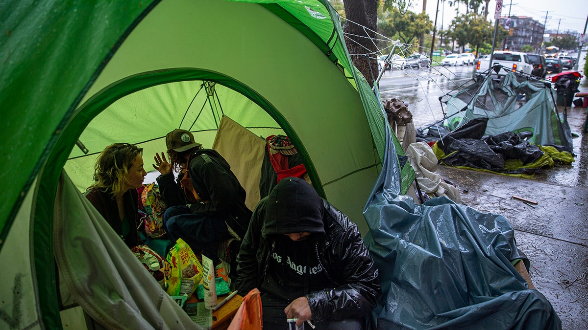 People try to stay warm as they face the elements inside a homeless encampment flooded under a rainstorm across the Echo Park Lake in Los Angeles, March 12, 2020. (Associated Press)