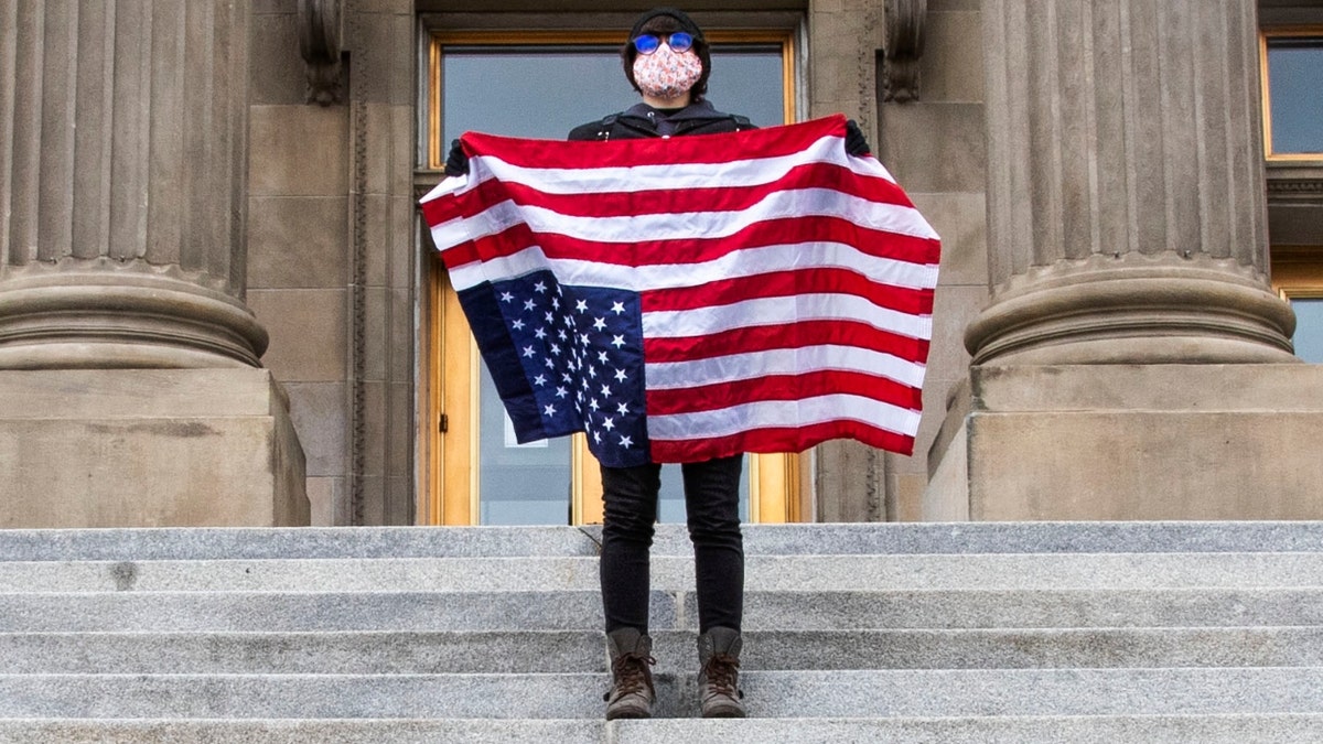 A student holding a U.S. Flag upside down stands atop the steps at the Idaho Capitol Building Monday, April 26, 2021 in Downtown Boise. (Darin Oswald /Idaho Statesman via AP)