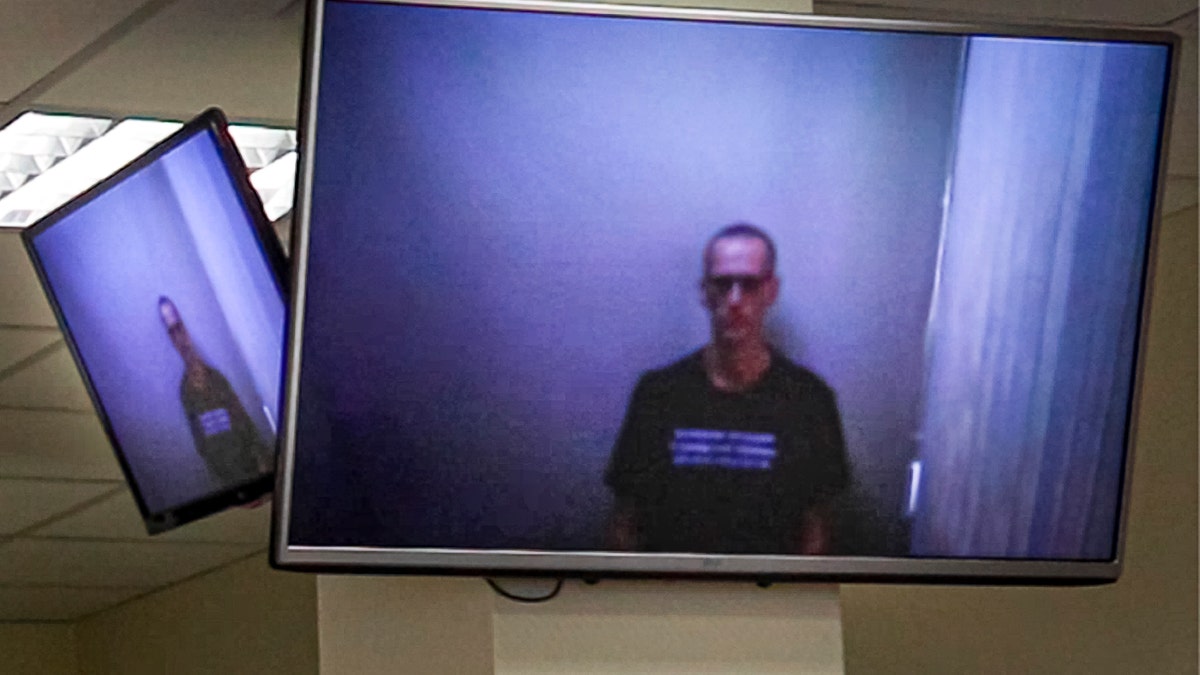 In this photo provided by the Babuskinsky District Court on Thursday, April 29, 2021, Russian opposition leader Alexei Navalny appears on TV screens via a video link from prison, during a hearing on his charges for defamation, in the Babuskinsky District Court in Moscow, Russia. The politician was convicted in February and ordered to pay a fine of 850-thousand rubles (the equivalent of $11,500). It was Navalny's first public appearance since his transfer to a penal colony last month. (Babuskinsky District Court Press Service via AP)