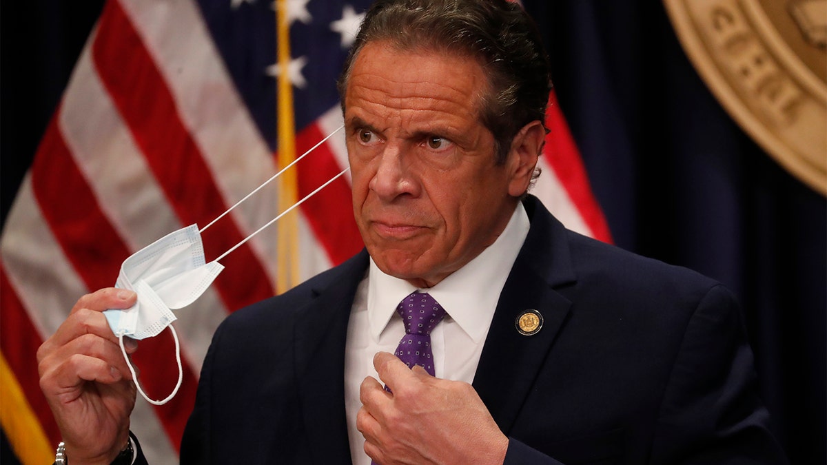 Gov. Andrew Cuomo takes off his face mask before a news conference in New York on Monday, April 19, 2021. (Shannon Stapleton/Pool via AP)