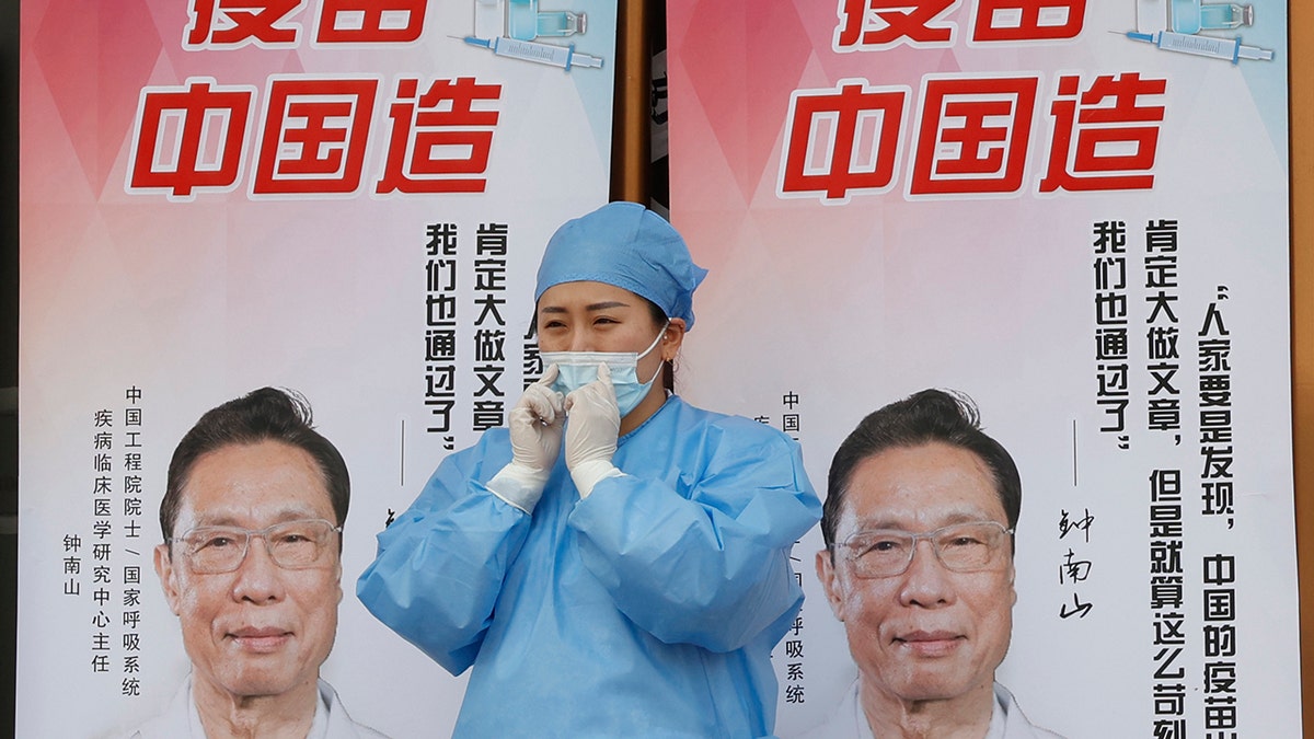 A medical worker adjusts her mask near propaganda boards showing famed Chinese medical expert Zhong Nanshan and the words "Vaccine China Made" outside vaccination center in Beijing Friday, April 9, 2021. (AP Photo/Ng Han Guan)