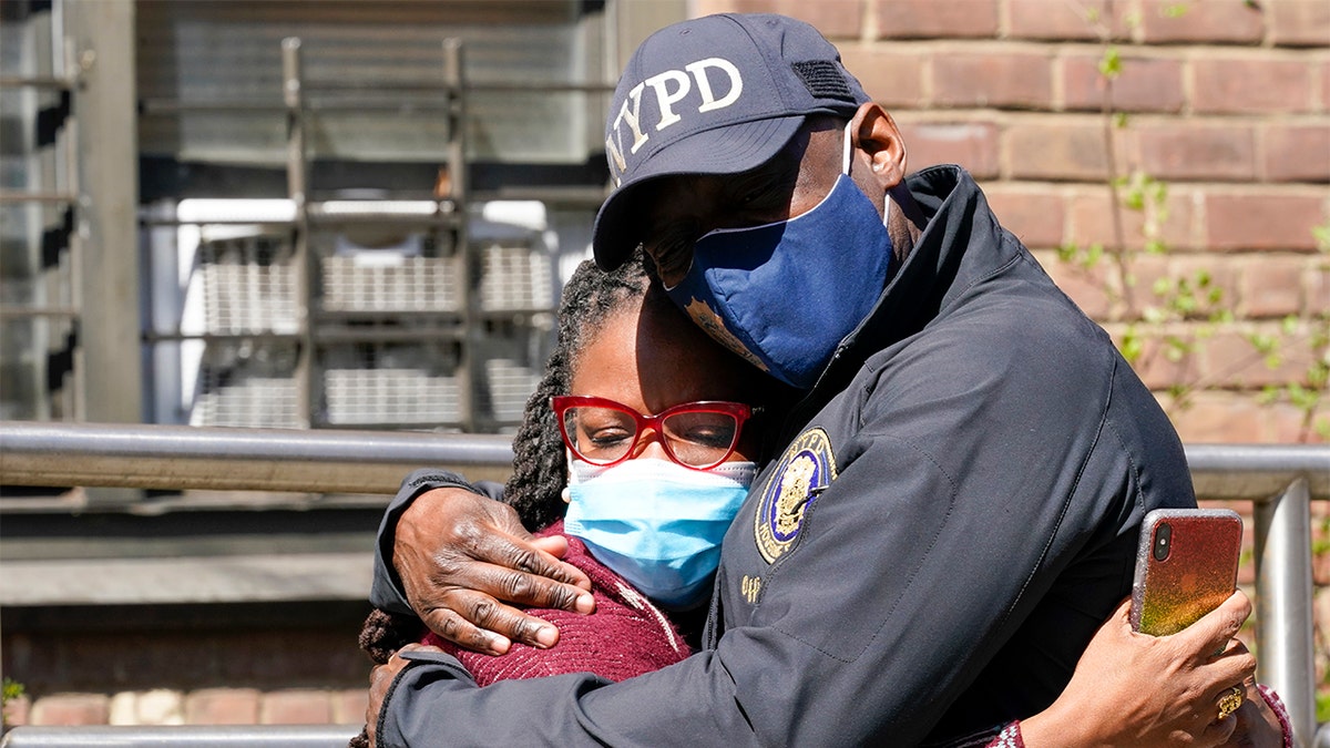A police officer hugs a community leader outside the building where a man shot the mother of his child and two of her daughters dead before turning the gun on himself, Tuesday, April 6, 2021. (AP Photo/Mary Altaffer)