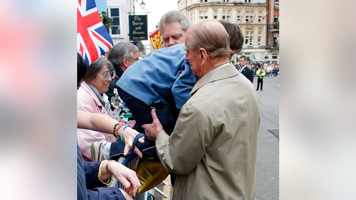 Prince Philip, Duke of Edinburgh lifts a young boy over the barriers as he and Queen Elizabeth II undertake a walkabout outside Windsor Castle to meet members of the public who have gathered on her 80th birthday on April 21, 2006, in Windsor, England.
