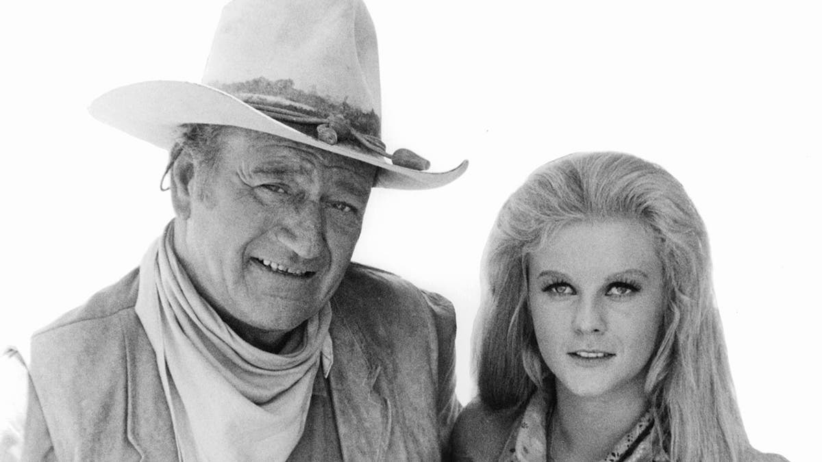 John Wayne holding Ann-Margret in publicity portrait for the film 'The Train Robbers', 1973.
