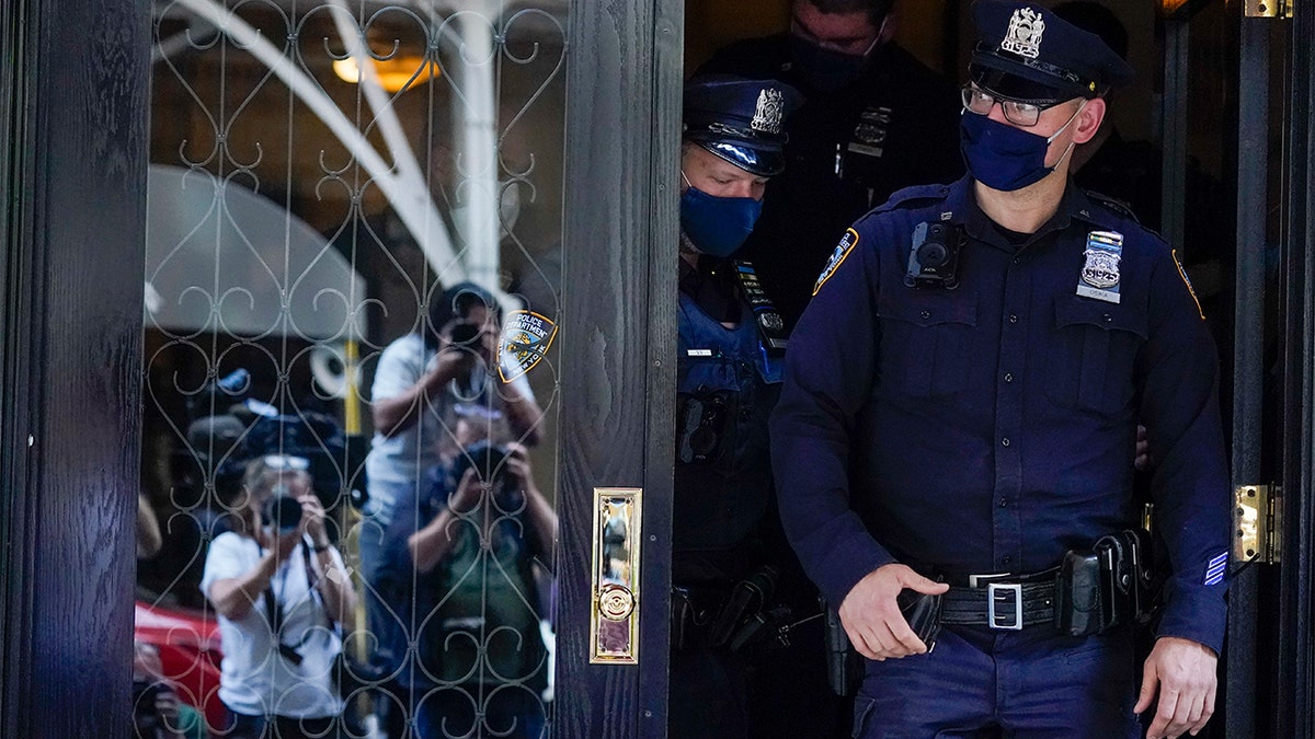 Members of the media are reflected in the widow a door as New York City Police officers walk out of the apartment building where former New York Mayor Rudy Giuliani resides, Wednesday, April 28, 2021, in New York.