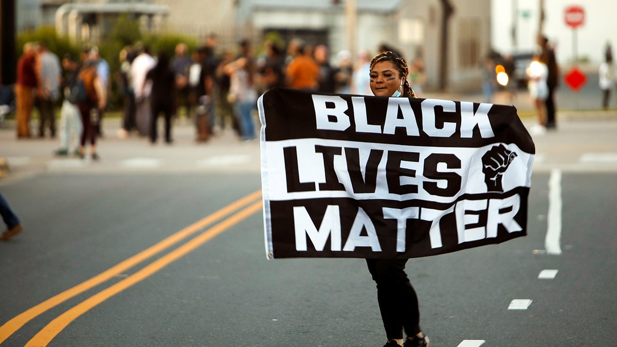 A protester carries a Black Lives Matter flag shortly before the start of a dawn to dusk curfew following the killing of Andrew Brown Jr. by sheriffs last week, in Elizabeth City, North Carolina, U.S. April 27, 2021. REUTERS/Jonathan Drake