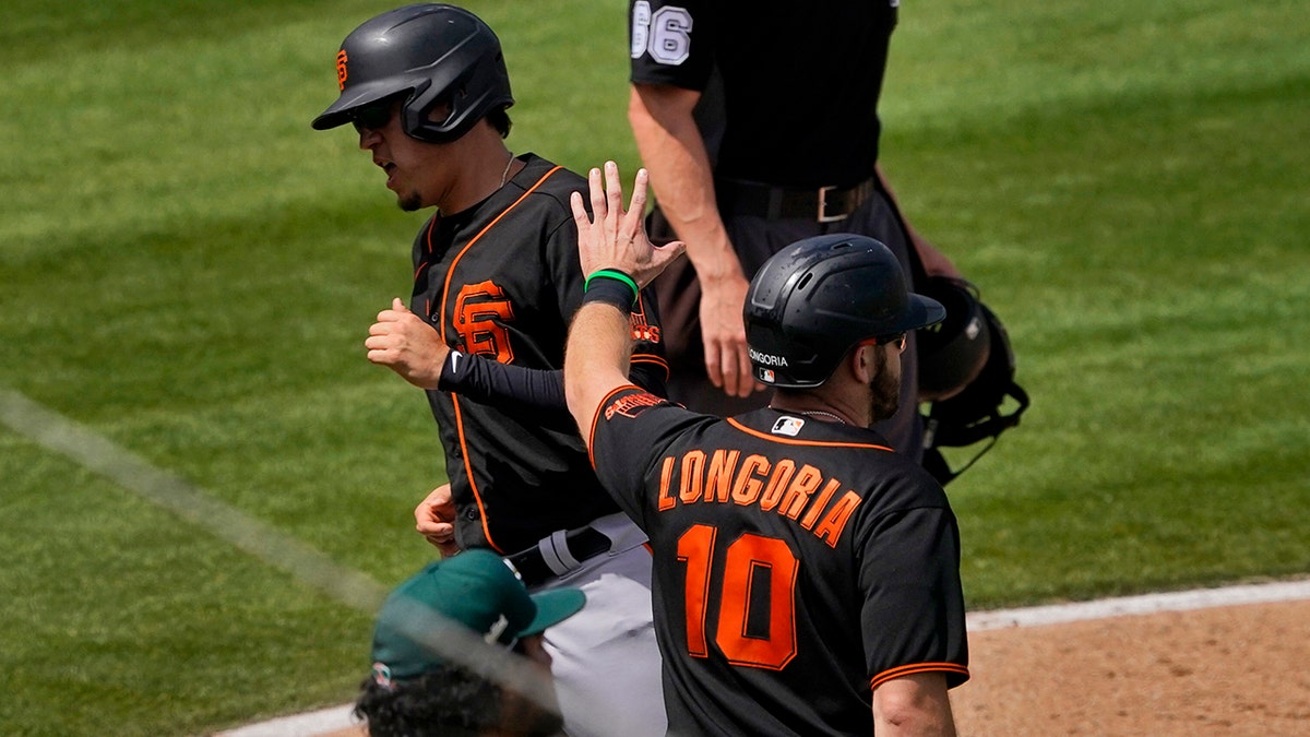 San Francisco Giants' Wilmer Flores and Evan Longoria (10) score on a double hit by Curt Casali during the third inning of a spring training baseball game against the Oakland Athletics, Monday, March 29, 2021, in Mesa, Ariz. (AP Photo/Matt York)