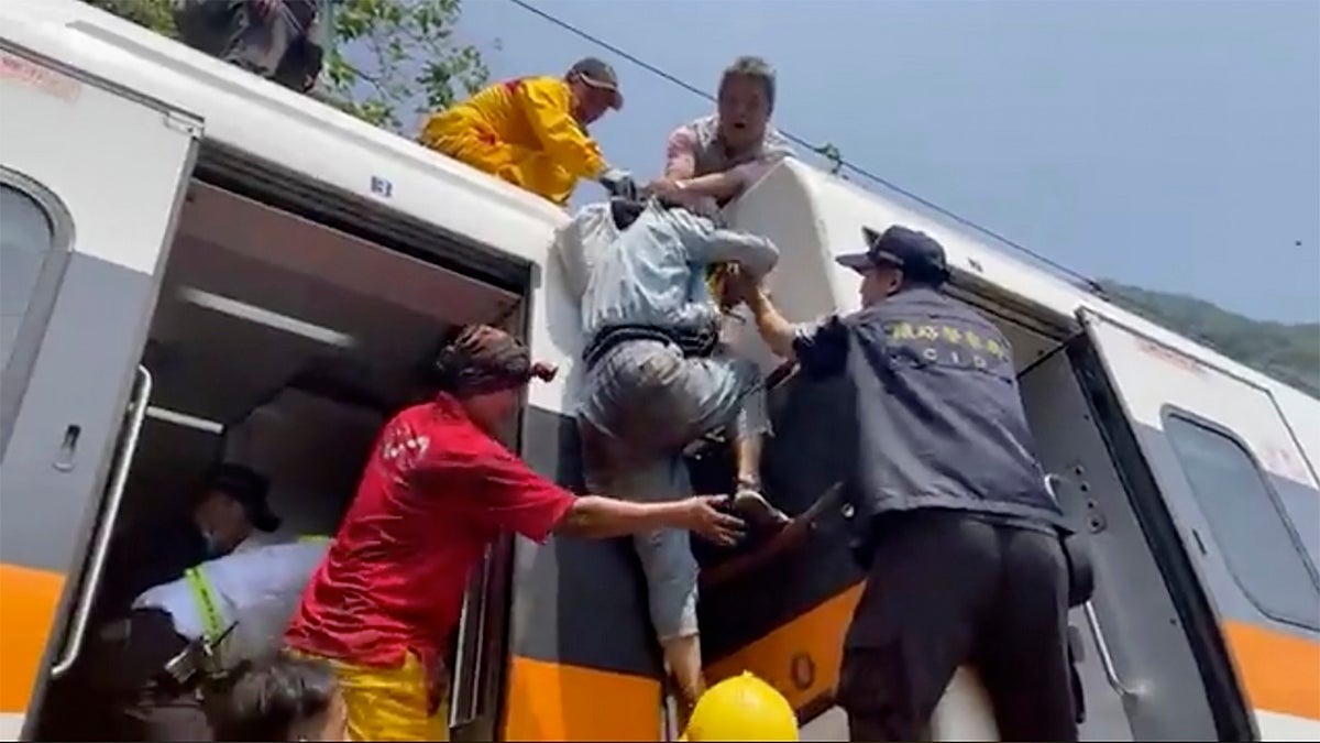 A passenger, center, is helped to climb out of the derailed train. (AP/hsnews.com.tw)