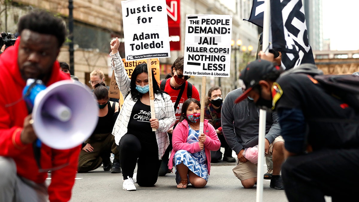 Abigail Garcia, 7, right, takes a knee with her mother Judith Garcia and other protestors during a peaceful protest on Tuesday, April 13, 2021, in downtown Chicago, demanding justice for Daunte Wright and Adam Toledo, who were shot dead by police. (AP Photo/Shafkat Anowar)