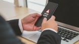 Business man hand is holding smart phone with scam alert warning sign.