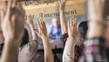 Rear view of group of students raising hands to answer teacher's question in the classroom. Focus is on hands in the middle.