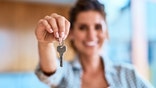 Portrait of a cheerful young woman holding the keys to her new home while standing inside during the day