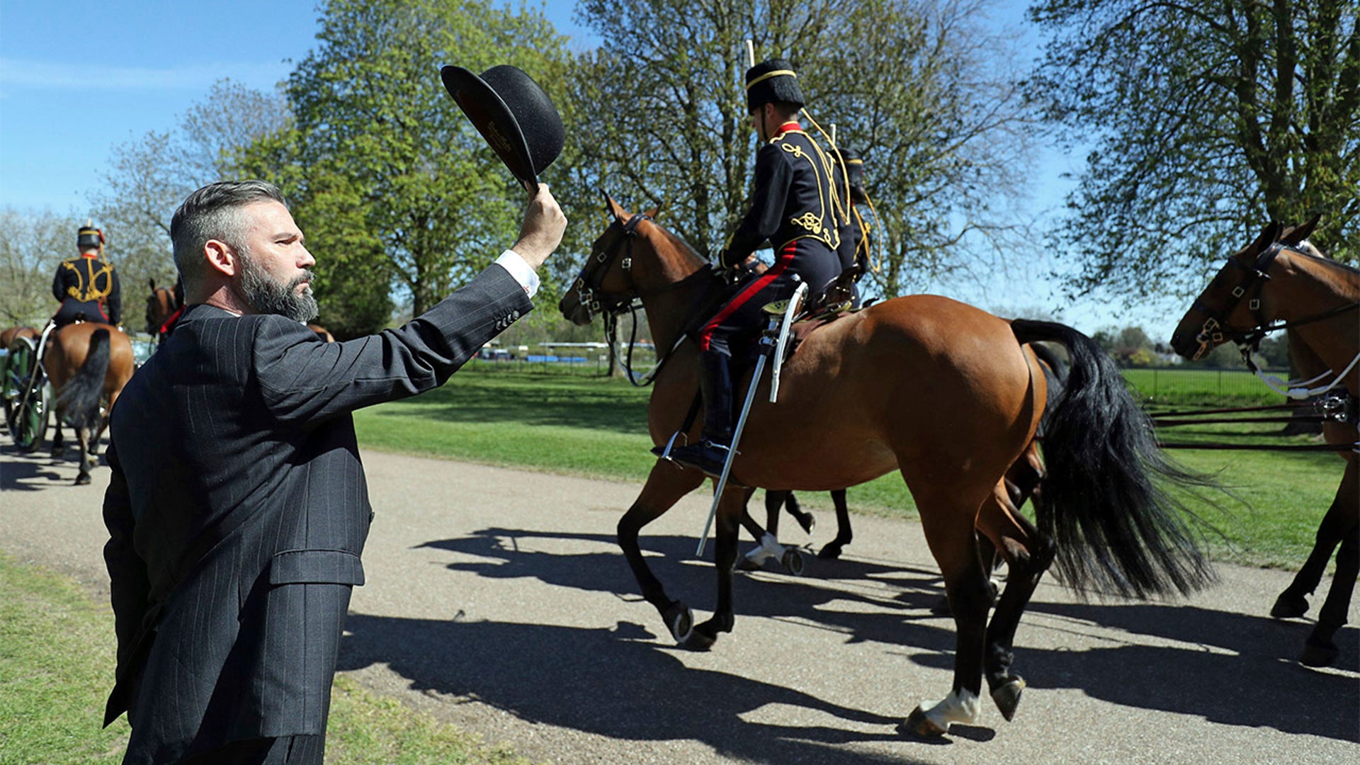 A man raises a bowler to The King's Troop Royal Horse Artillery as they ride toward Windsor Castle in Windsor, England, on Saturday, April 17, 2021, ahead of the funeral of Britain's Prince Philip. Prince Philip died April 9 at the age of 99 after 73 years of marriage to Queen Elizabeth II. (Andrew Matthews/PA via AP)