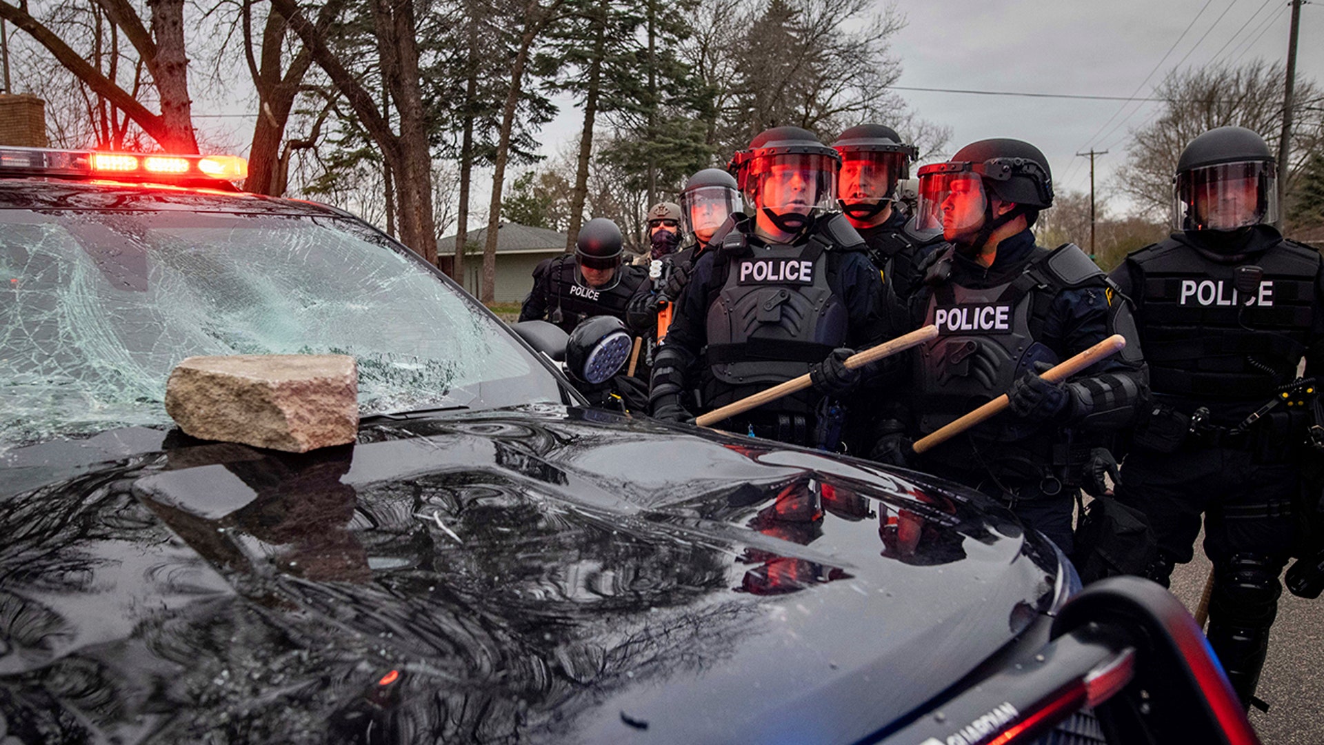 Police stand near a police cruiser after a rock was thrown at it in protest, Sunday, April 11, 2021, in Brooklyn Center, Minnesota. The family of Daunte Wright, 20, told a crowd that he was shot by police Sunday before getting back into his car and driving away, then crashing the vehicle several blocks away. The family said Wright was later pronounced dead.