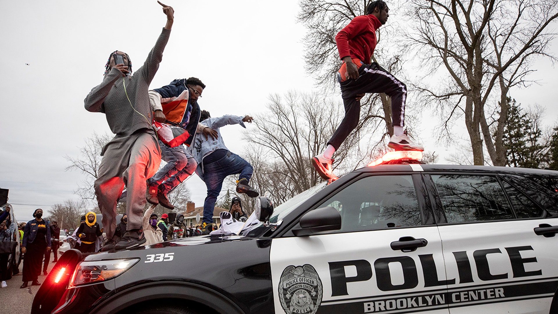 Men jump on police vehicles near the site of a shooting involving a police officer, Sunday, April 11, 2021, in Brooklyn Center, Minnesota.