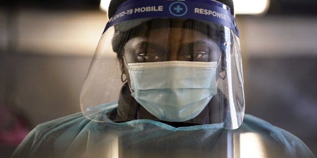 In this Dec. 8, 2020, file photo, a health care worker wears personal protective equipment as she speaks to a patient at a mobile testing location for COVID-19 in Auburn, Maine. (AP Photo/Robert F. Bukaty, File)