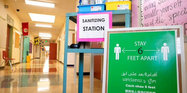A sanitizing station and sign encouraging social distancing sits in the main hallway during the first day of partial in-person instruction at an elementary school in California.