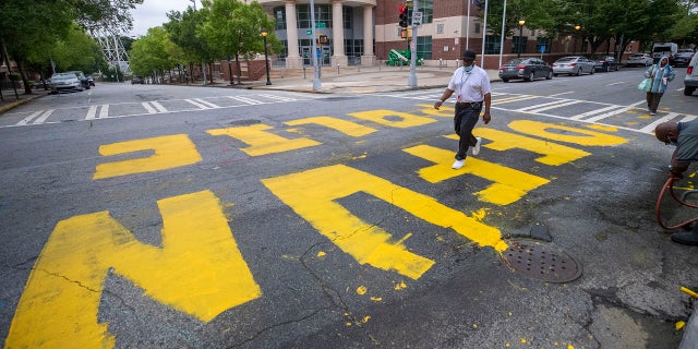 FILE - In this Wednesday, June 10, 2020, file photo, a man walk across a "Defund Police" written in front of the Atlanta Police Department Headquarters. (Alyssa Pointer/Atlanta Journal-Constitution via AP)