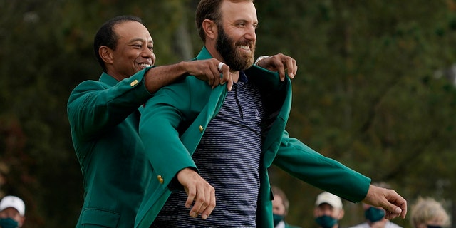 Tiger Woods helps Masters' champion Dustin Johnson with his green jacket after his victory at the Masters golf tournament in Augusta, Georgia, in this Sunday, Nov. 15, 2020, file photo.
