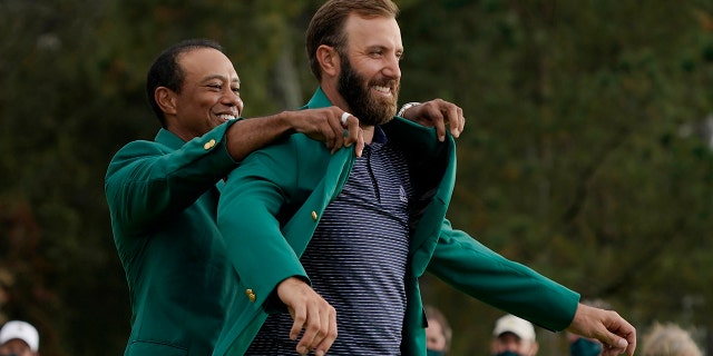 Tiger Woods helps Masters' champion Dustin Johnson with his green jacket after his victory at the Masters golf tournament in Augusta, Georgia, in this Sunday, Nov. 15, 2020, file photo.