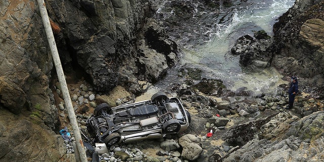 Bodega Bay firefighters are working to secure the scene of an accident after a vehicle from the Bodega Head car park in Bodega Bay, California, fell through a wooden barrier, landed left and upside down 100 feet to the rocky shore and two people in the SUV, Saturday, April 3, 2021. (Kent Porter / The Press Democrat via AP)