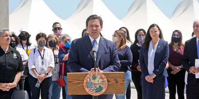 Florida Gov. Ron DeSantis, center, speaks during a news conference surrounded by officials and cruise workers, Thursday, April 8, 2021, at PortMiami in Miami. DeSantis announced a lawsuit against the federal government and the CDC demanding that cruise ships be allowed to sail. (AP Photo/Wilfredo Lee)