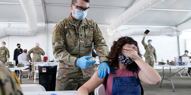 Leanne Montenegro, 21, covers her eyes as she doesn't like the sight of needles, while she receives the Pfizer COVID-19 vaccine at a FEMA vaccination center at Miami Dade College, Monday, April 5, 2021, in Miami. (AP Photo/Lynne Sladky)