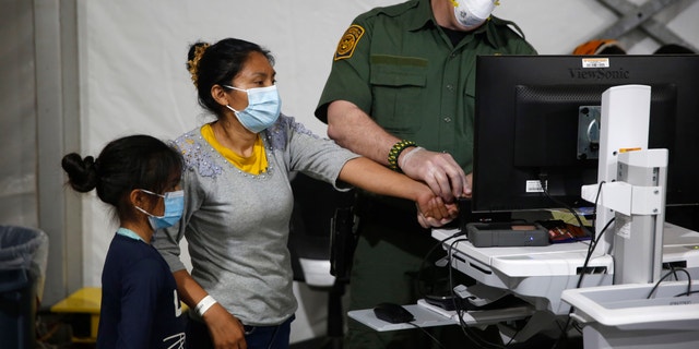 A migrant and her daughter have their biometric data entered at the intake area of the U.S. Department of Homeland Security holding facility, the main detention center for unaccompanied children in the Rio Grande Valley, in Donna, Texas, March 30, 2021.