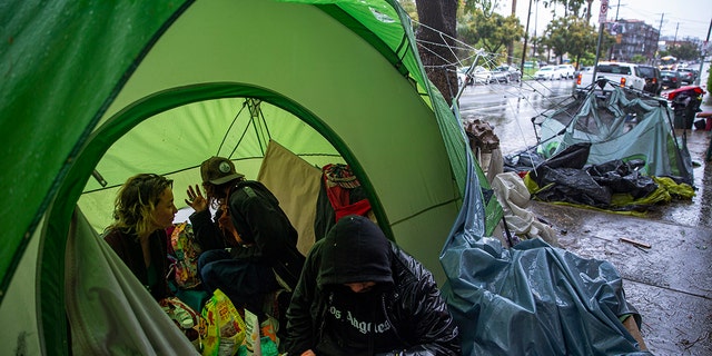People try to stay warm as they face the elements inside a homeless encampment flooded under a rainstorm across the Echo Park Lake in Los Angeles, March 12, 2020. (Associated Press)