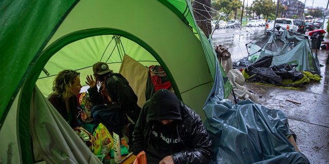 People try to stay warm as they face the elements inside a homeless encampment flooded under a rainstorm across the Echo Park Lake in Los Angeles, March 12, 2020. (Associated Press)