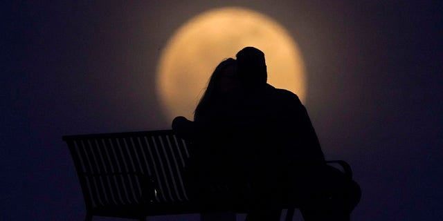 A couple watch the moon rise from from a park, Monday, April 26, 2021, in New Albany, Ind. This moon is a supermoon, meaning it appears larger than an average full moon because it is nearer the closest point of its orbit to Earth. (AP Photo/Charlie Riedel)