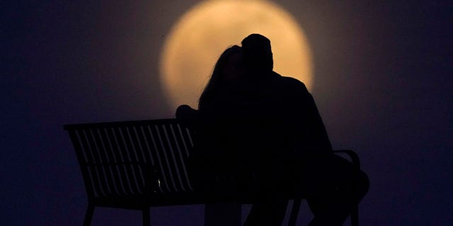 A couple watch the moon rise from from a park, Monday, April 26, 2021, in New Albany, Ind. This moon is a supermoon, meaning it appears larger than an average full moon because it is nearer the closest point of its orbit to Earth. (AP Photo/Charlie Riedel)