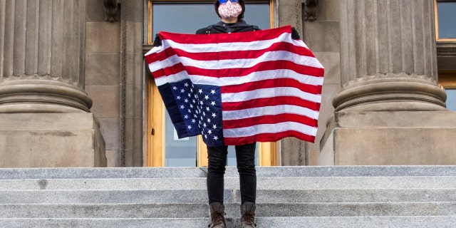 A student holding a U.S. Flag upside down stands atop the steps at the Idaho Capitol Building Monday, April 26, 2021 in Downtown Boise. (Darin Oswald /Idaho Statesman via AP)